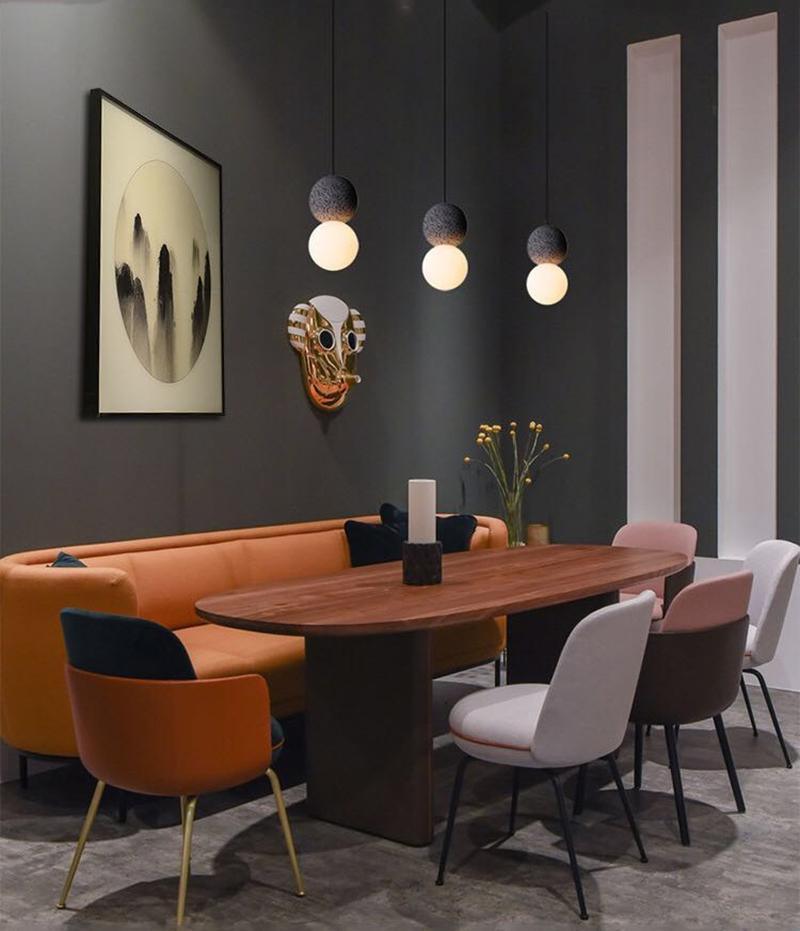 Three Clérachic pendants hang above a dining table with a burnt-orange banquette and dusty-pink chairs.