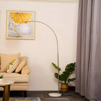 A Clérachic arc floor lamp with a white dome shade curves over a cream armchair near a window with mauve curtains.