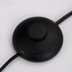 Close-up of the round black inline foot switch on the power cord of a Clérachic arc floor lamp.