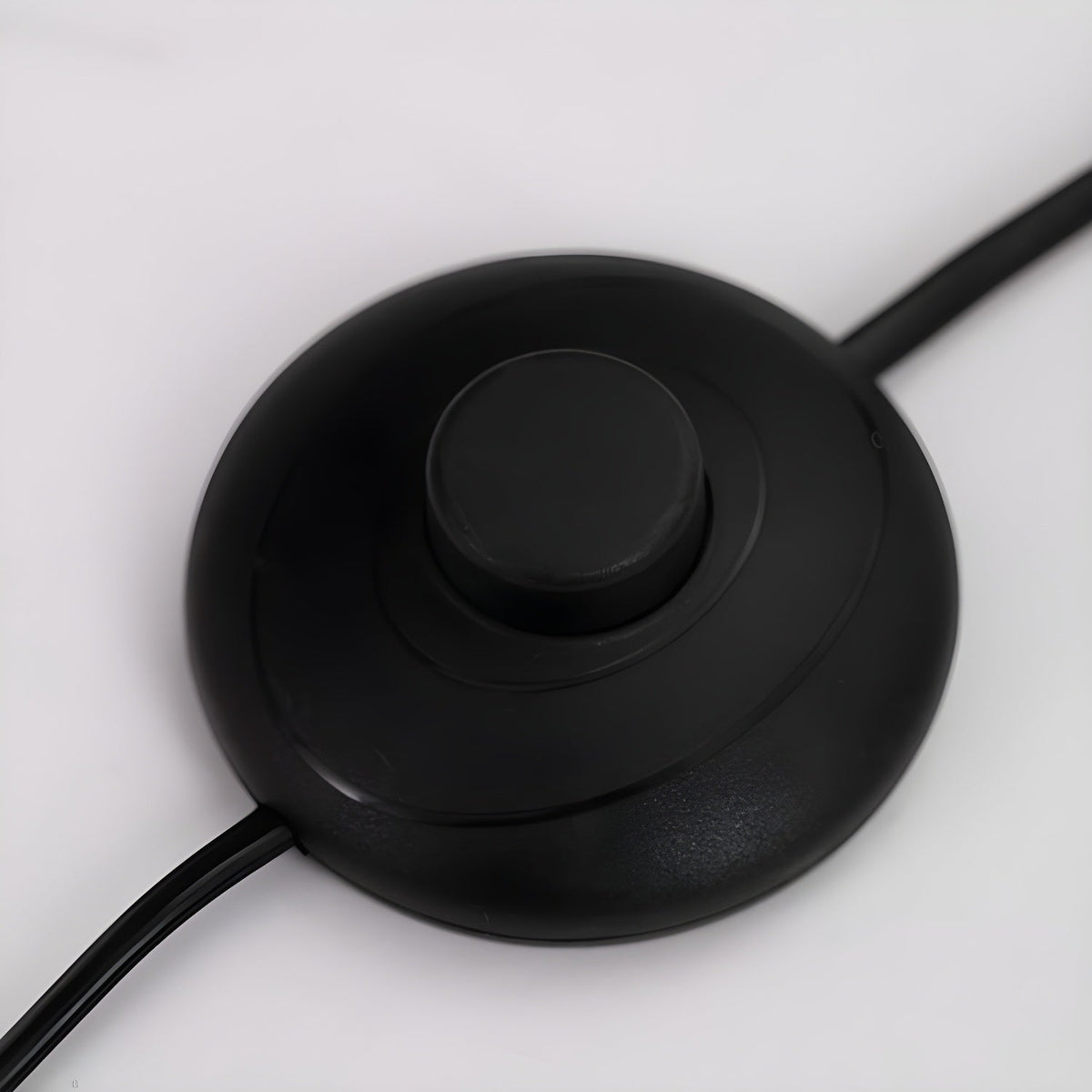 Close-up of the round black inline foot switch on the power cord of a Clérachic arc floor lamp.