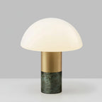 Studio shot of a Clérachic domed glass table lamp with a green marble base and brushed gold stem, lit against grey.