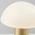 Close-up from below of a Clérachic domed table lamp's lit glass shade meeting its brushed gold stem.