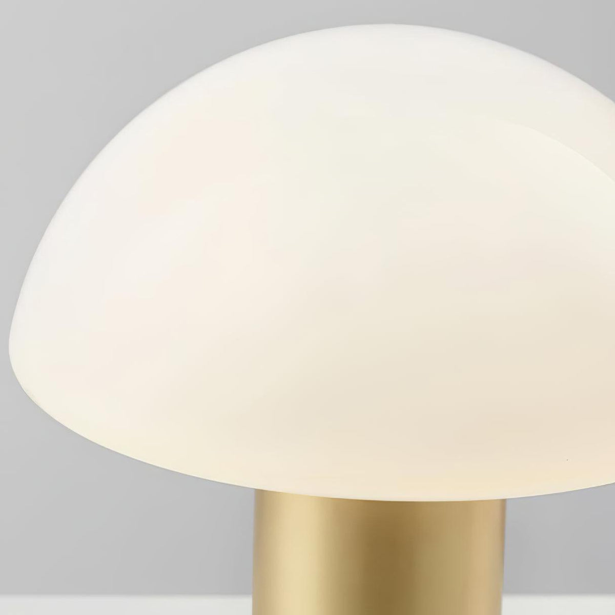 Close-up from below of a Clérachic domed table lamp's lit glass shade meeting its brushed gold stem.