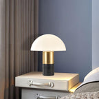 A Clérachic domed table lamp with a dark marble base glows on a bedside table between a navy wall and beige curtain.