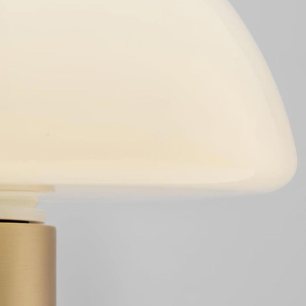Extreme close-up, softly blurred, of a Clérachic domed table lamp's glass shade edge and brushed gold neck.