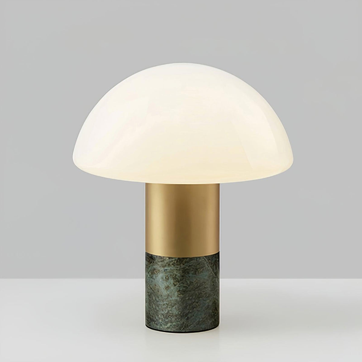 Studio shot of a Clérachic domed glass table lamp with a green marble base, centred against a grey gradient backdrop.