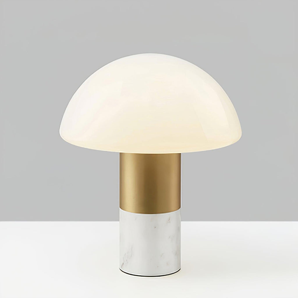 Studio shot of a Clérachic domed glass table lamp with a white marble base and brushed gold stem, lit against a grey backdrop.