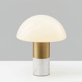 Studio shot of a Clérachic domed glass table lamp with a white marble base and brushed gold stem, lit against a grey backdrop.