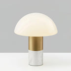 Studio shot of a Clérachic domed glass table lamp with a white marble base and brushed gold stem, lit against a grey backdrop.