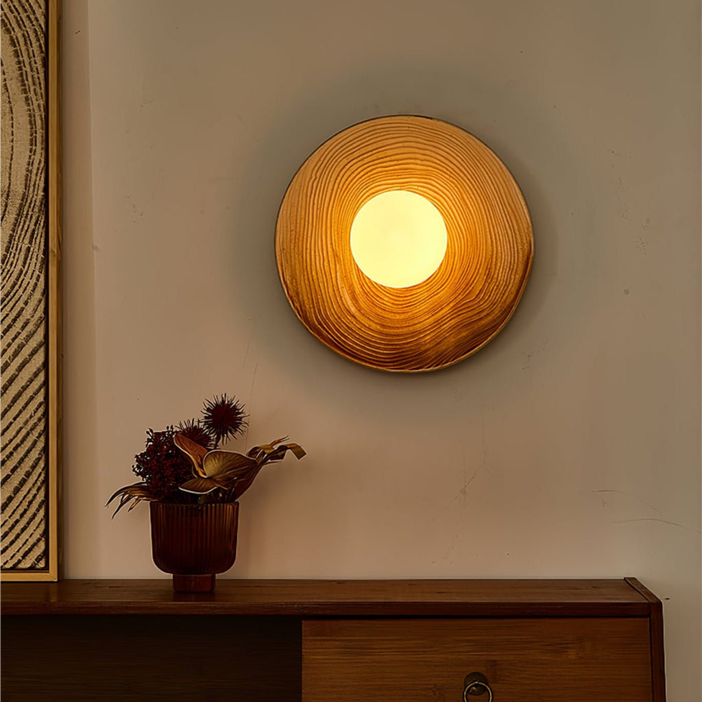 A Clérachic ceramic wall sconce glows warm amber in a dim room, above a sideboard holding a copper vase of dried thistles.