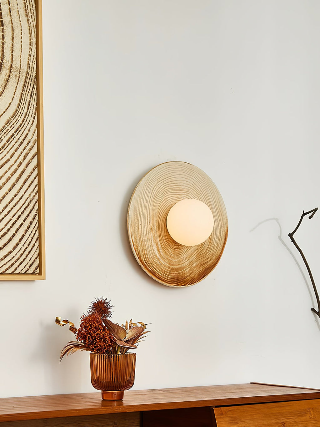 A lit Clérachic ceramic circle sconce seen from across a room, mounted above a walnut sideboard beside framed wall art.