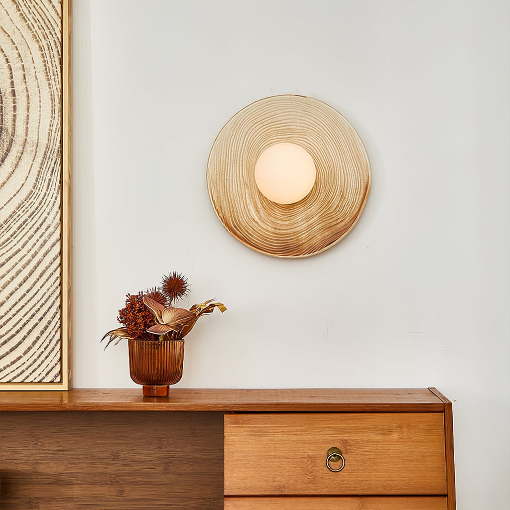Clérachic's ceramic circle sconce lights a plaster wall above a walnut sideboard with dried thistles in a copper vase.