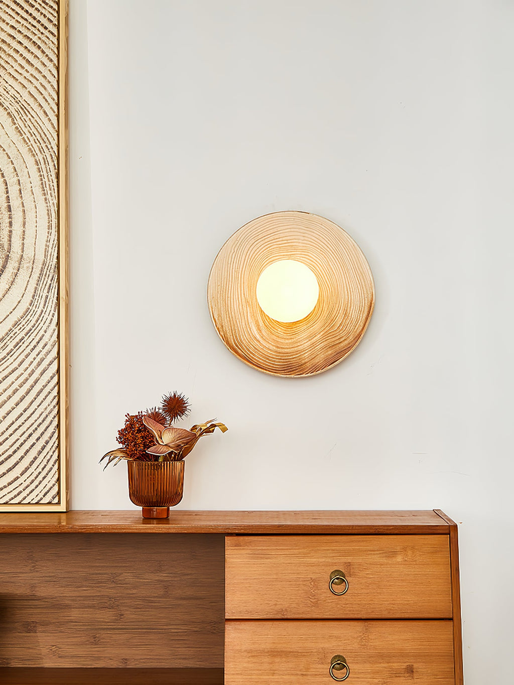 A closer view of the Clérachic ceramic wall sconce glowing above a walnut sideboard, beside a textured wood-grain print.