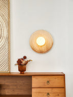 A closer view of the Clérachic ceramic wall sconce glowing above a walnut sideboard, beside a textured wood-grain print.