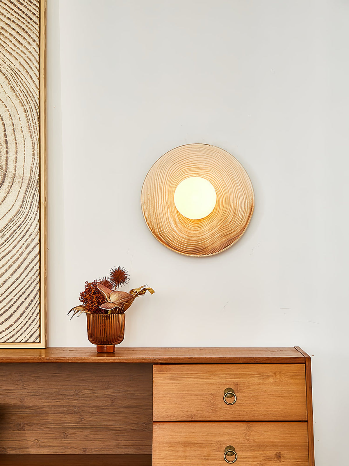 A closer view of the Clérachic ceramic wall sconce glowing above a walnut sideboard, beside a textured wood-grain print.