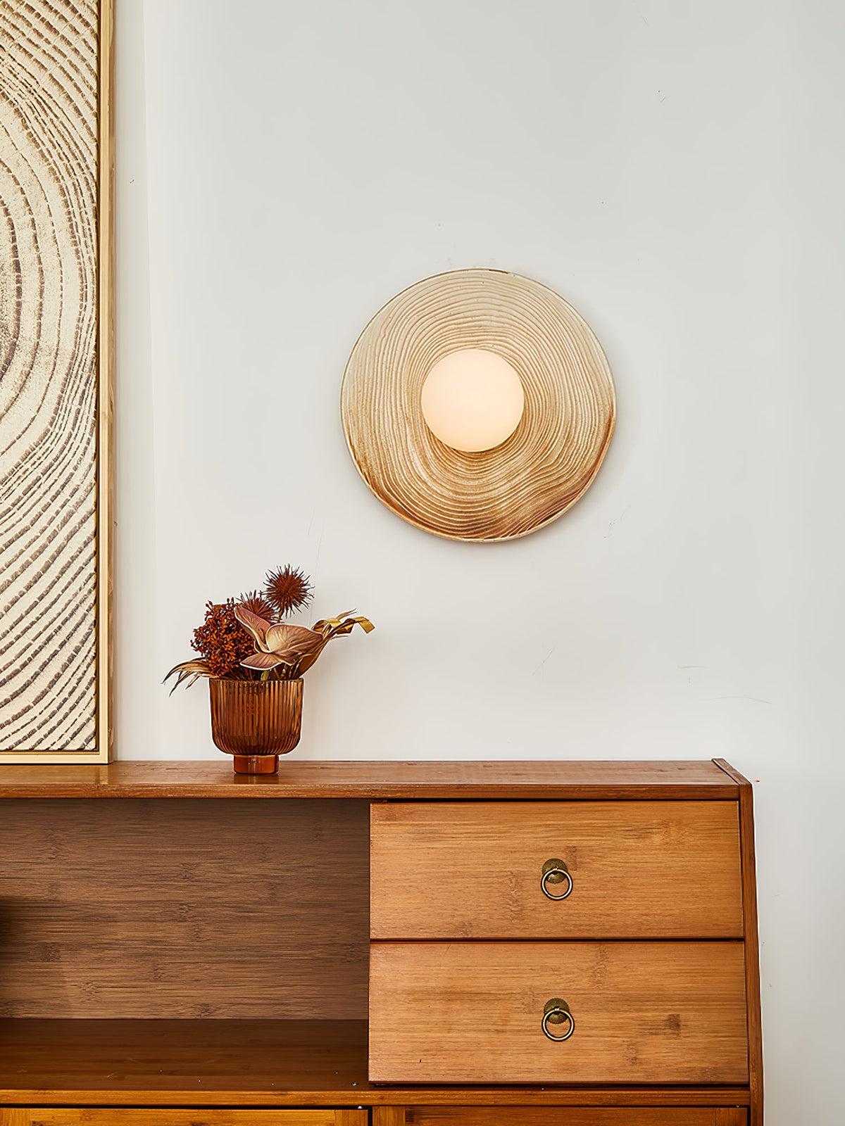 The Clérachic ceramic circle sconce lit above a sideboard, with a bare curved branch standing beside the dried arrangement.