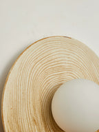 Close-up of the ridged terra-beige ceramic disc on a Clérachic wall sconce, its opal globe set low against the grooved texture.