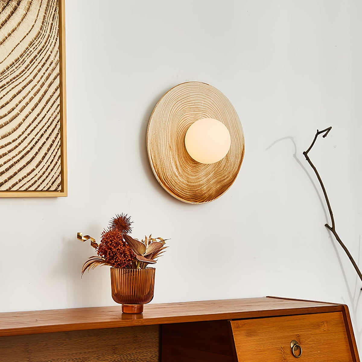A Clérachic ceramic wall sconce glows above a walnut sideboard, its curved branch prop casting a thin shadow on the wall.