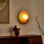 In dim evening light, a Clérachic ceramic circle sconce glows warm amber above a sideboard with dried florals in a copper vase.