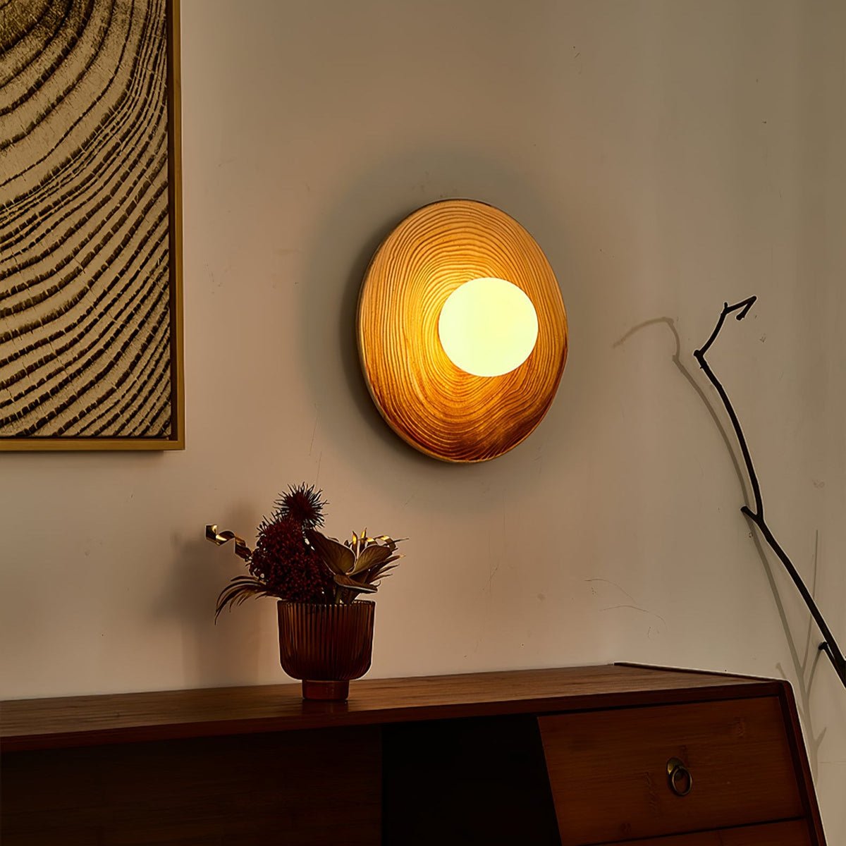 In dim evening light, a Clérachic ceramic circle sconce glows warm amber above a sideboard with dried florals in a copper vase.