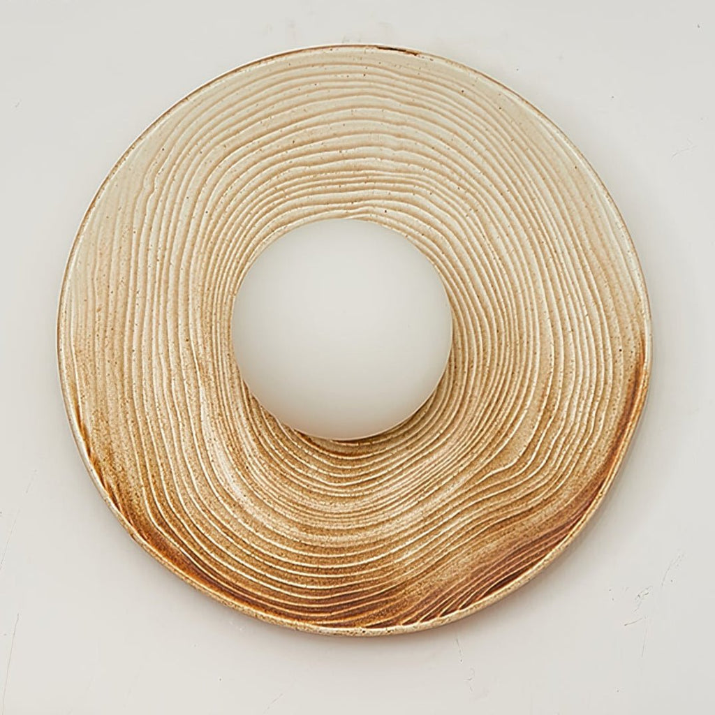 A wide close-up of the ridged terra-beige ceramic ring from a Clérachic wall sconce, its centre opening left bare of the globe.