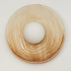 A wide close-up of the ridged terra-beige ceramic ring from a Clérachic wall sconce, its centre opening left bare of the globe.