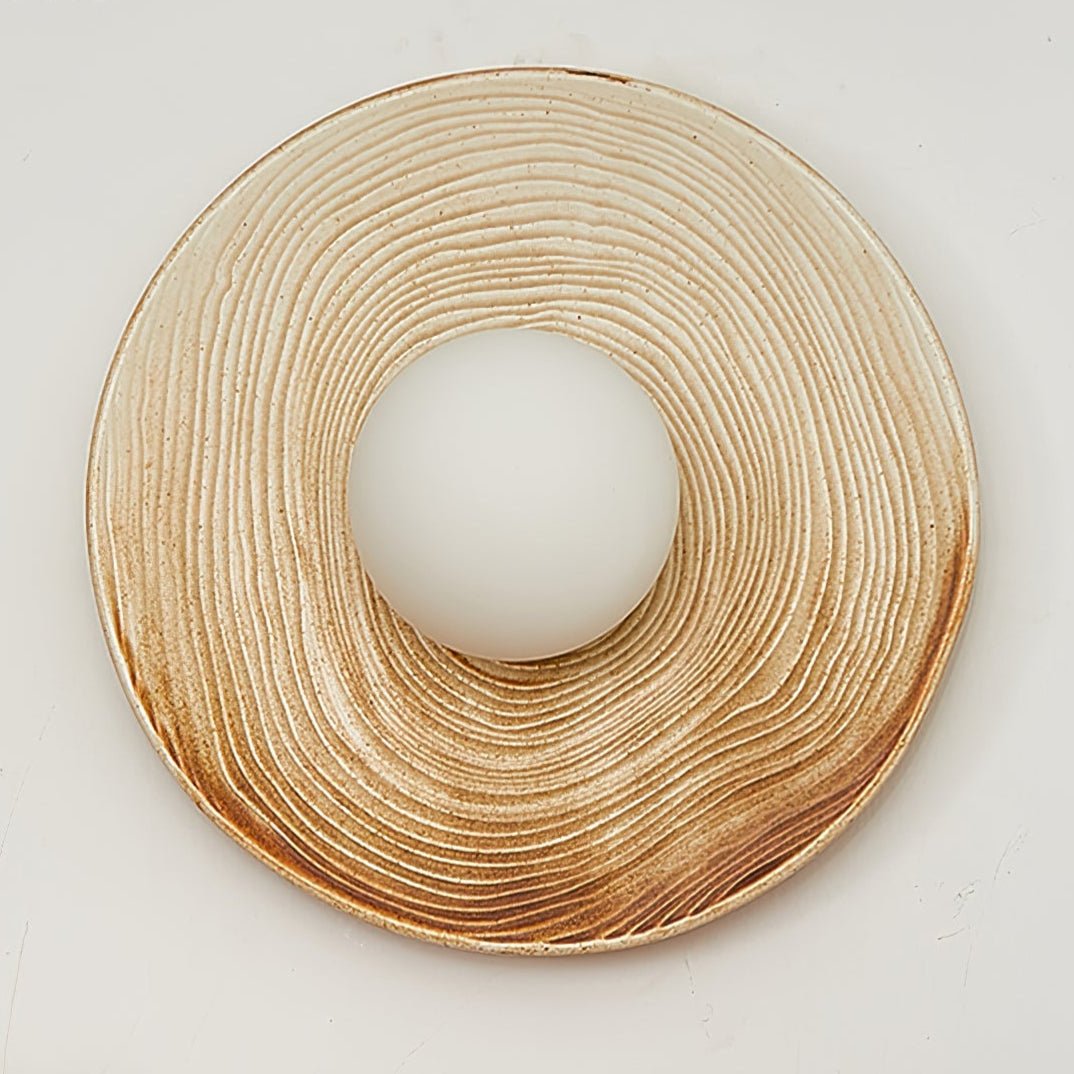 A wide close-up of the ridged terra-beige ceramic ring from a Clérachic wall sconce, its centre opening left bare of the globe.