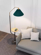 Clérachic floor lamp beside a grey sofa with white pillows, green pleated shade lit above a wood tray with a phone, chequered rug at the base.