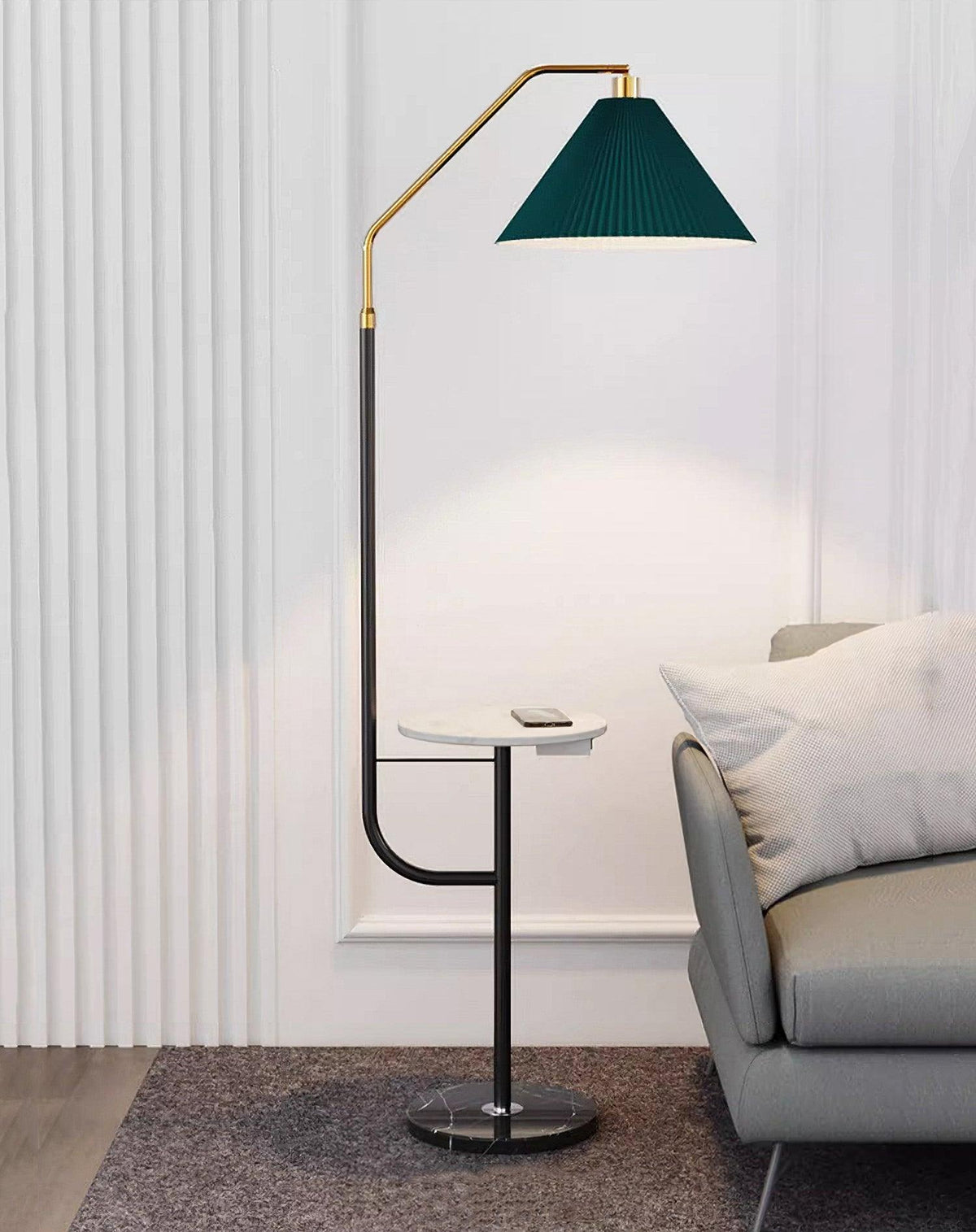 Clérachic floor lamp beside a panelled wall, green pleated shade lit above a marble tray holding a phone, more of the grey wall in view.