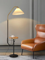 Clérachic floor lamp beside a burnt-orange leather chair, cream pleated shade glowing above a wood tray set with a cup and saucer.