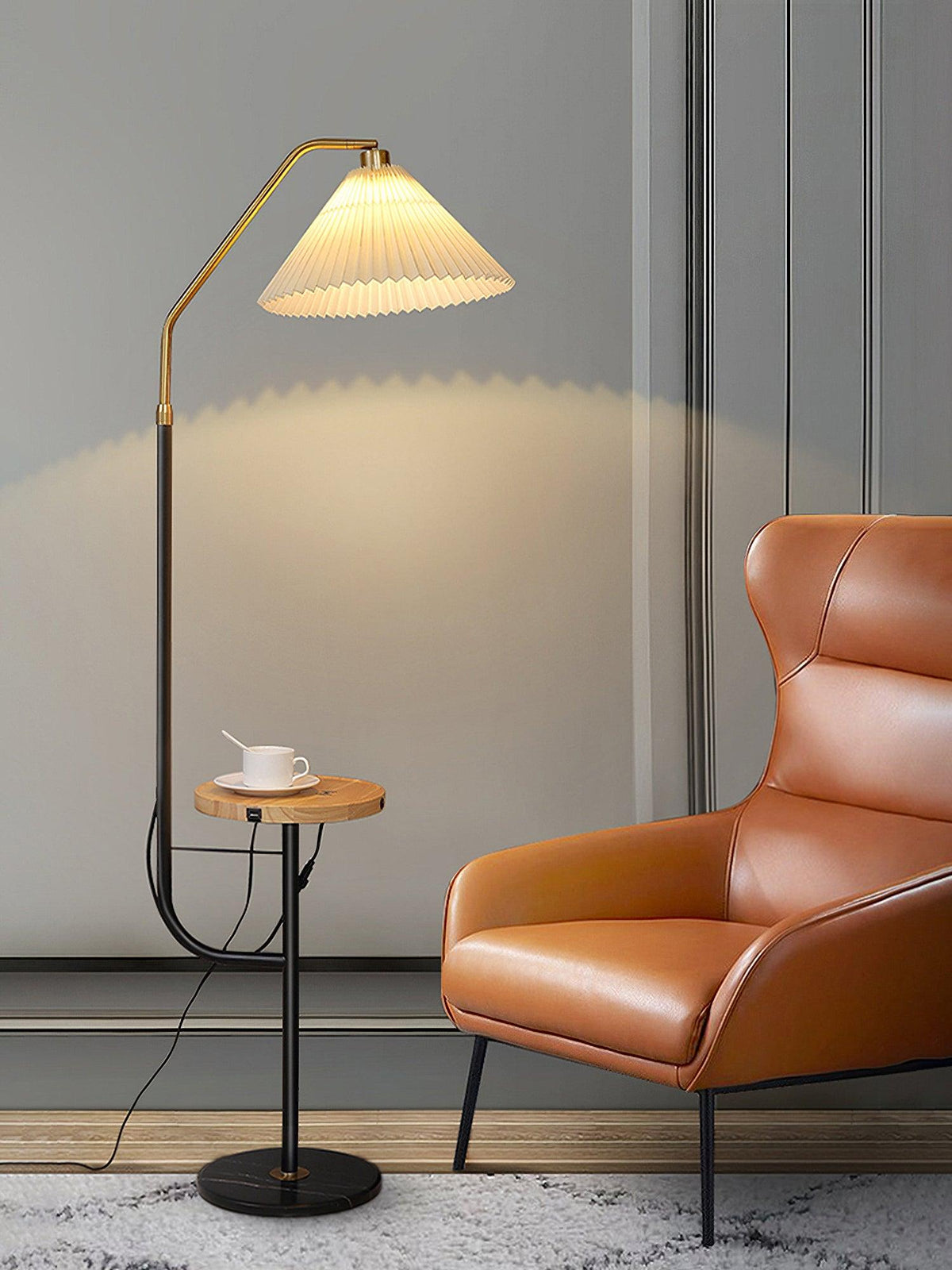 Clérachic floor lamp beside a burnt-orange leather chair, cream pleated shade glowing above a wood tray set with a cup and saucer.