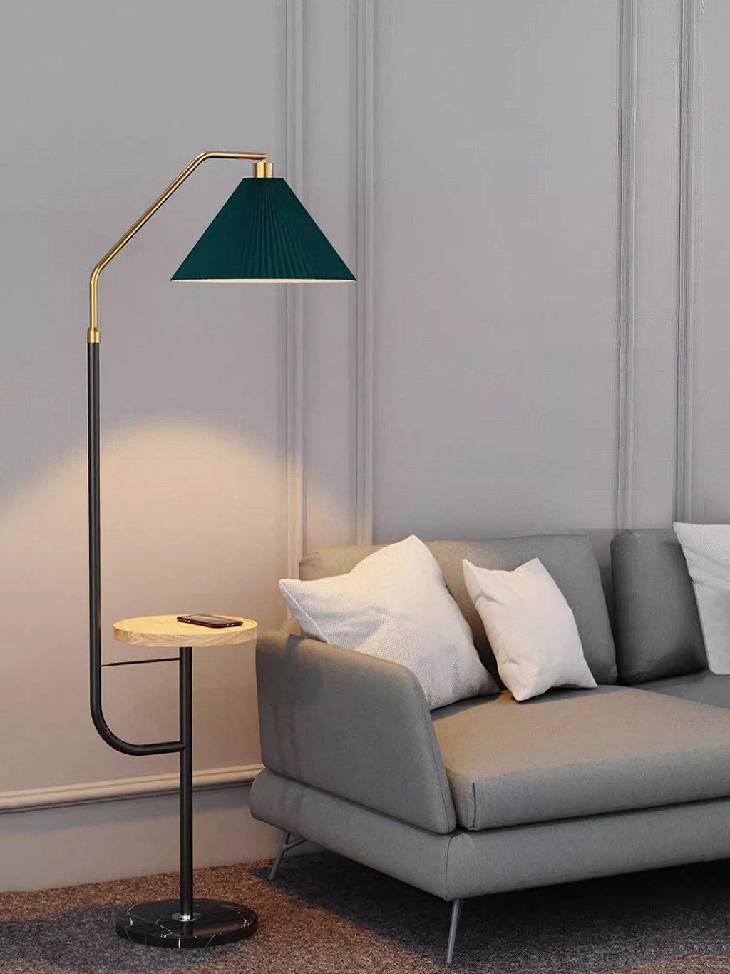 Clérachic floor lamp beside a grey sofa with white pillows, green pleated shade lit above a wood tray holding a phone, panelled wall behind.