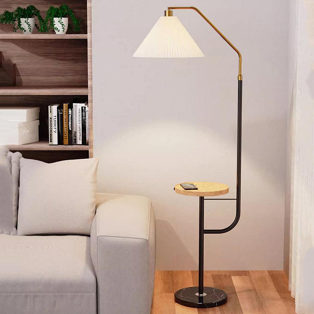 Clérachic floor lamp against a bookshelf of books and storage boxes, cream pleated shade lit above a wood tray holding a phone.