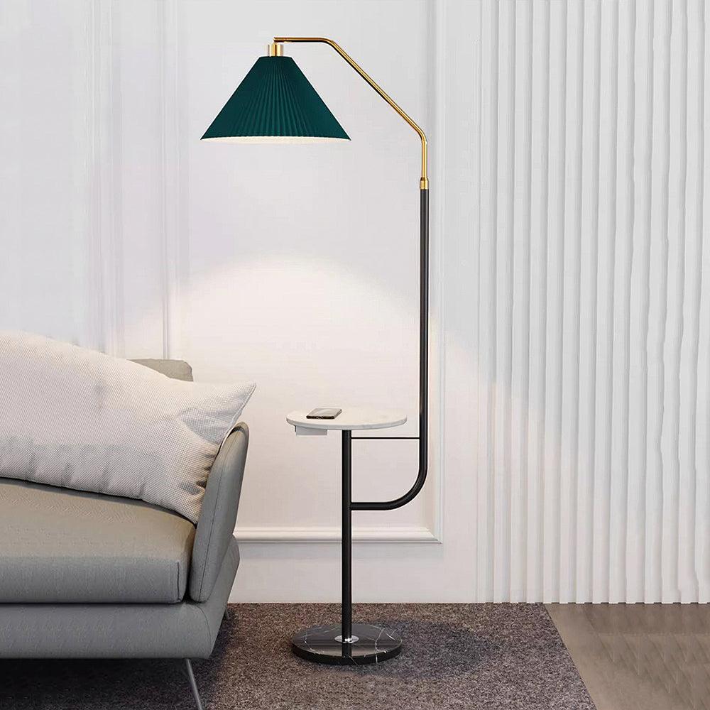 Clérachic floor lamp beside a grey sofa on a rug, green pleated shade lit above a white tray table, set against a panelled white wall.