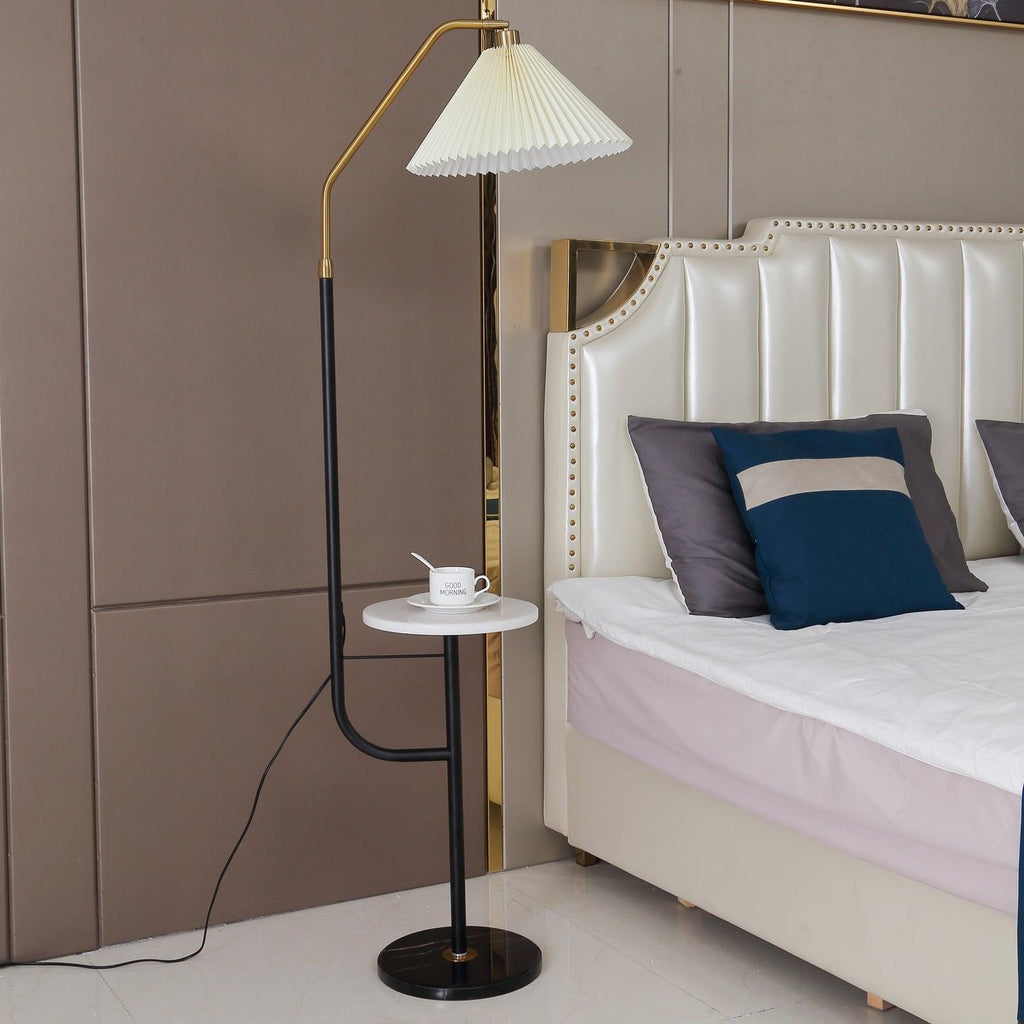 Clérachic floor lamp shown full length beside the same studded headboard, cream shade lit above a marble tray with a cup and saucer.