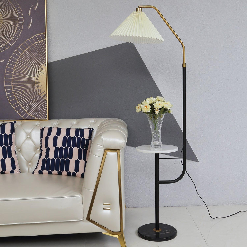 Clérachic floor lamp beside a tufted cream leather sofa, cream pleated shade lit above a marble tray topped with a small vase of yellow roses.