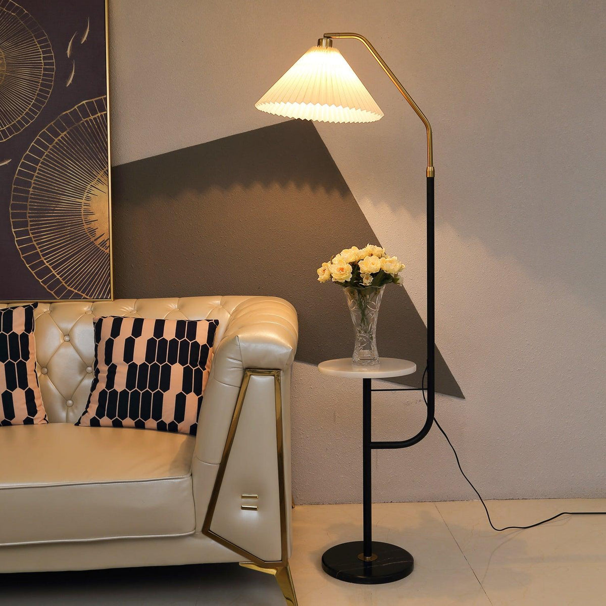 Clérachic floor lamp beside a tufted cream leather sofa with brass legs, cream shade lit above a marble tray topped with a small vase of yellow roses.