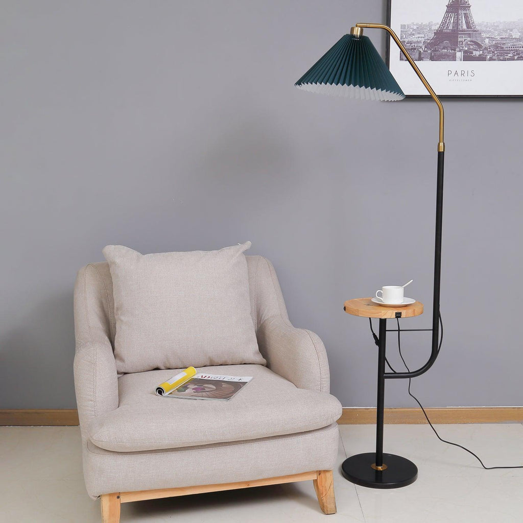 Clérachic floor lamp beside a beige armchair under a framed Paris print, green pleated shade lit above a wood tray set with a cup and saucer.