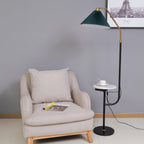 Clérachic floor lamp beside a beige armchair with a magazine on the seat, green pleated shade above a marble tray set with a cup and saucer.