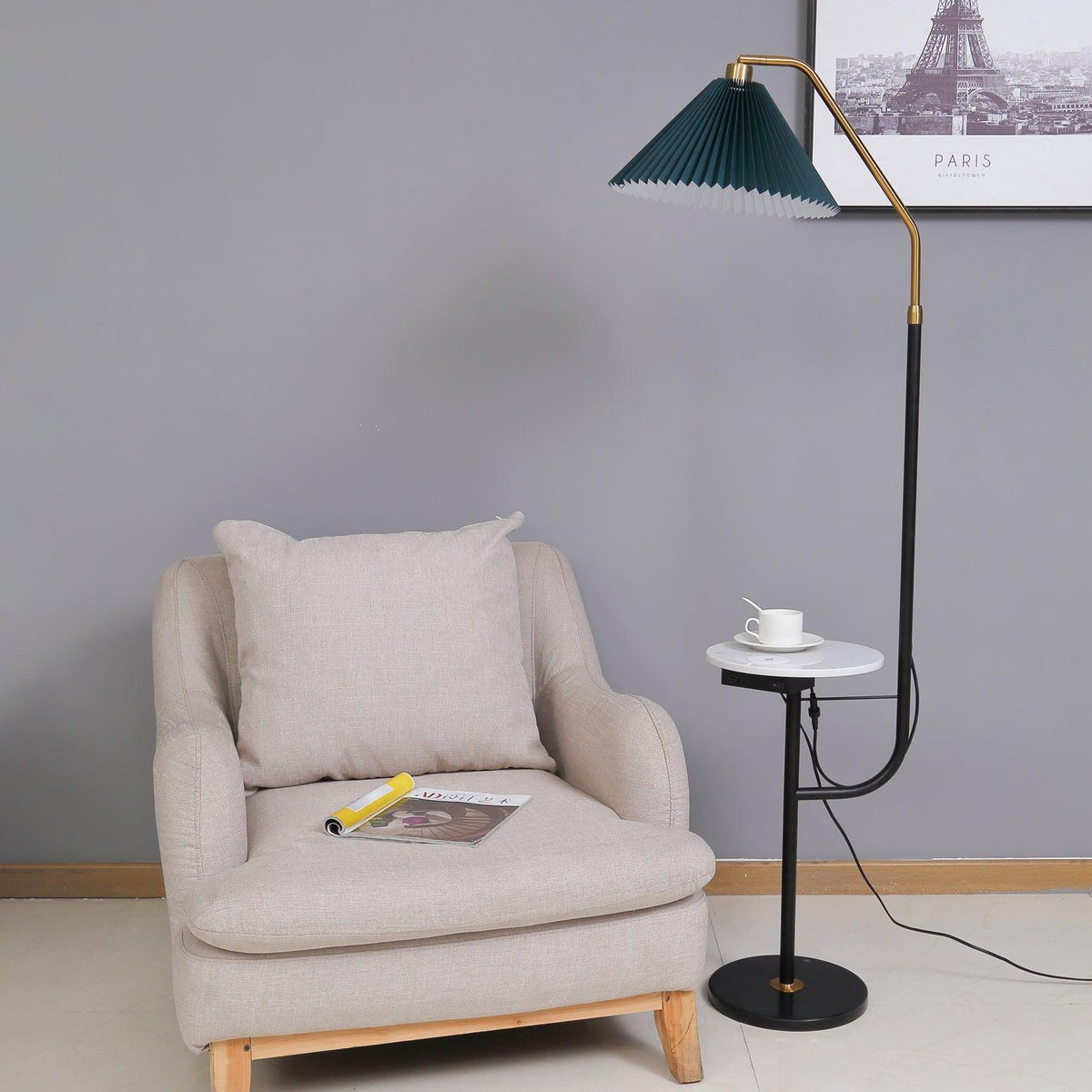 Clérachic floor lamp beside a beige armchair with a magazine on the seat, green pleated shade above a marble tray set with a cup and saucer.