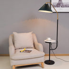 Clérachic floor lamp lit beside a beige armchair and a magazine, green pleated shade above a marble tray set with a cup and saucer.