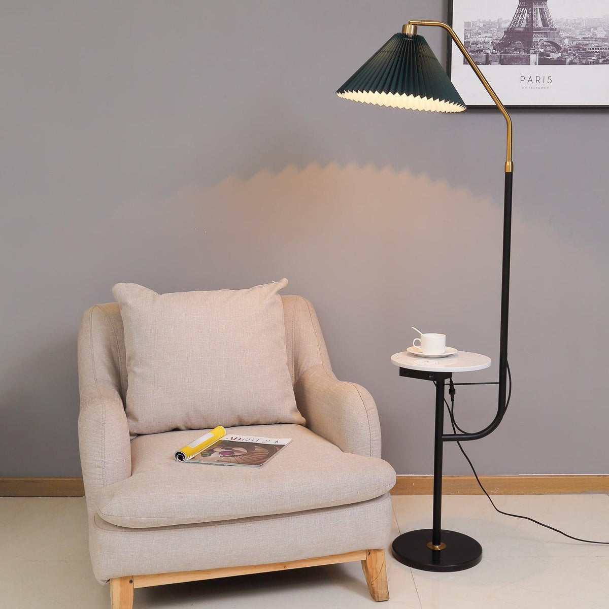 Clérachic floor lamp lit beside a beige armchair and a magazine, green pleated shade above a marble tray set with a cup and saucer.