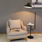 Clérachic floor lamp beside a beige armchair, dark green pleated shade lit under a framed Paris print, marble tray holding a cup and saucer.