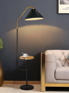 Clérachic floor lamp against a dark navy wall, green pleated shade lit above a wood tray holding a teacup, framed art visible in the corner.