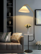 Clérachic floor lamp beside a brown leather sofa with patterned cushions, cream shade lit above a marble tray topped with white flowers.