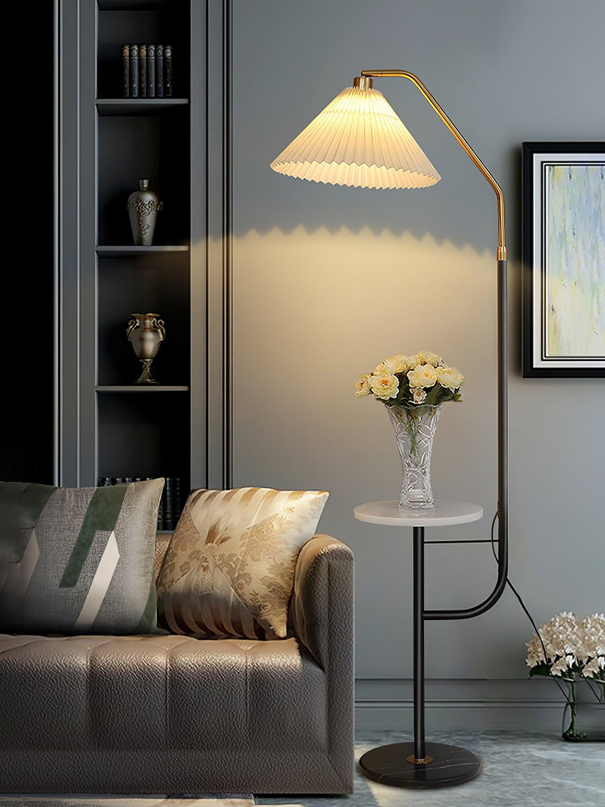 Clérachic floor lamp beside a brown leather sofa with patterned cushions, cream shade lit above a marble tray topped with white flowers.