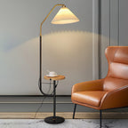 Clérachic floor lamp beside a burnt-orange leather wingback chair, cream pleated shade lit above a wood tray set with a cup and saucer.