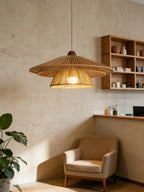 Beside an upholstered armchair, this Clérachic pendant glows warm above open wood shelving lined with pottery.