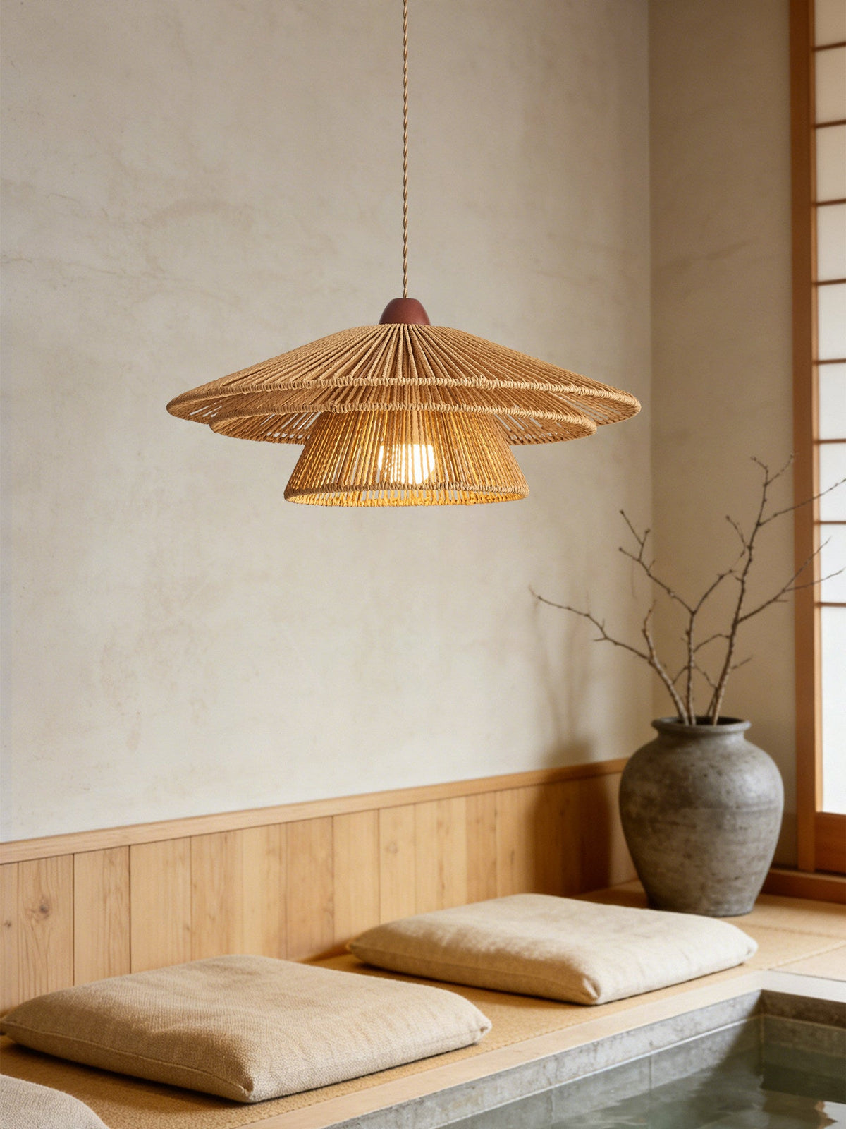 Floor cushions sit beneath this Clérachic pendant's warm glow, beside a large stoneware vase.