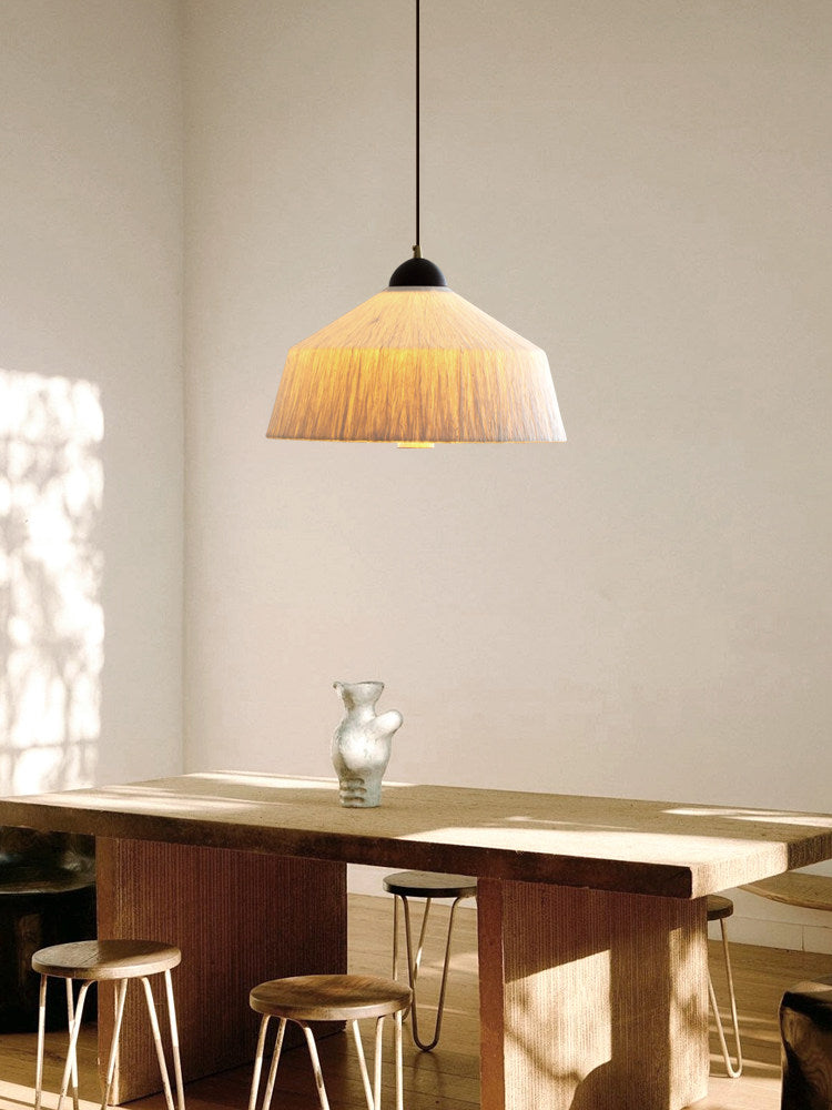 Sunlight streaks across a wood table and stools beneath this Clérachic pendant's beige rice paper shade, glowing warm.